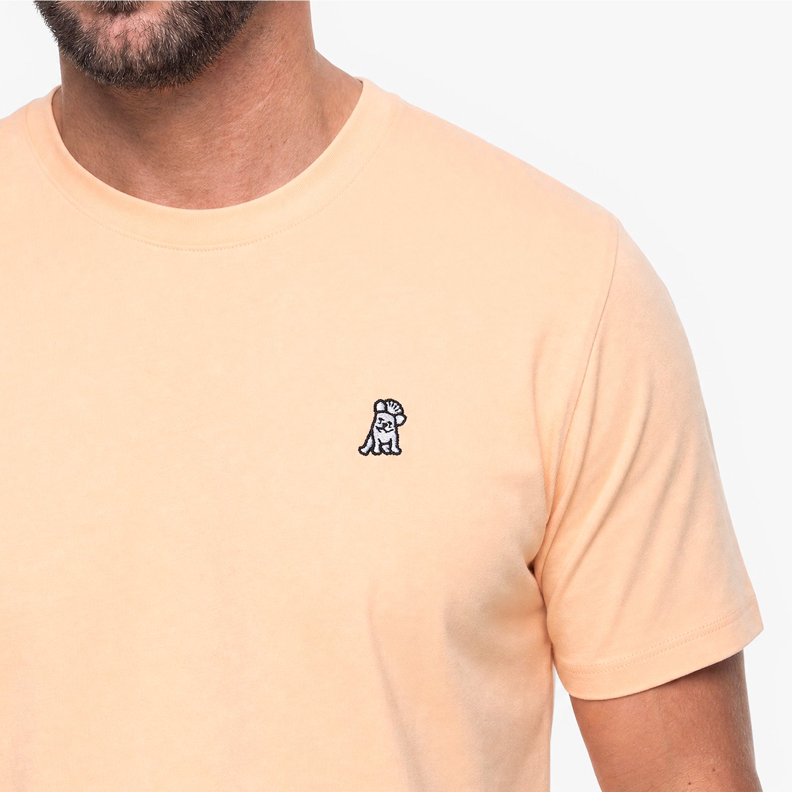 Beige t-shirt with a small logo on the chest against a white background