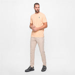 Man wearing a light peach t-shirt and beige pants on a white background