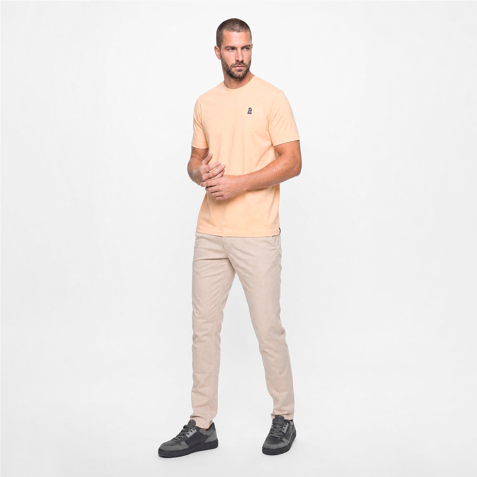 Man wearing a light peach t-shirt and beige pants on a white background