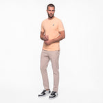 Man wearing a peach t-shirt and beige pants on a white background