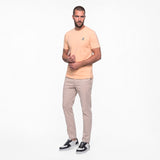 Man wearing a peach t-shirt and beige pants on a white background