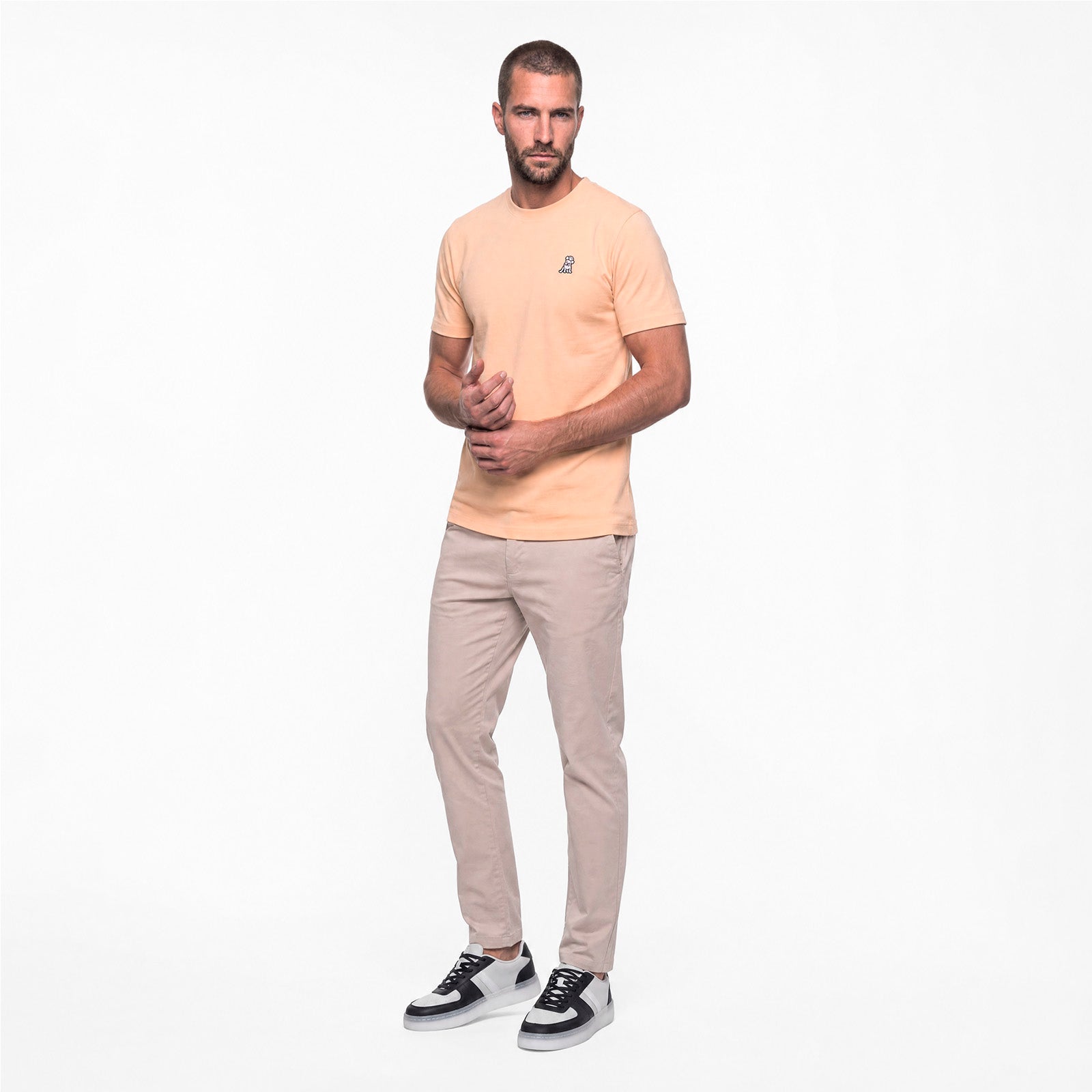 Man wearing a peach t-shirt and beige pants on a white background