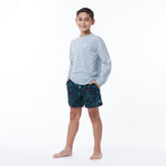 Full body picture of a child wearing a light blue long-sleeve shirt and patterned shorts on a white background