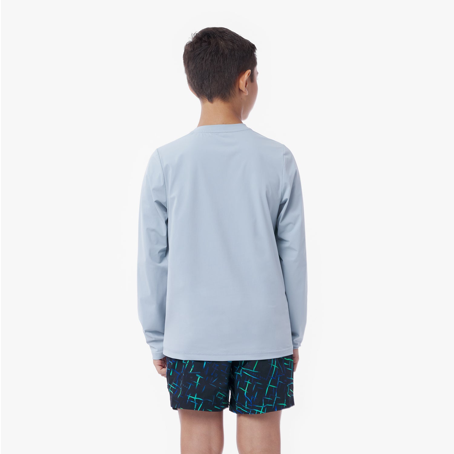 Back picture of a child wearing a light blue long-sleeve rashguard and dark shorts with a pattern on a white background