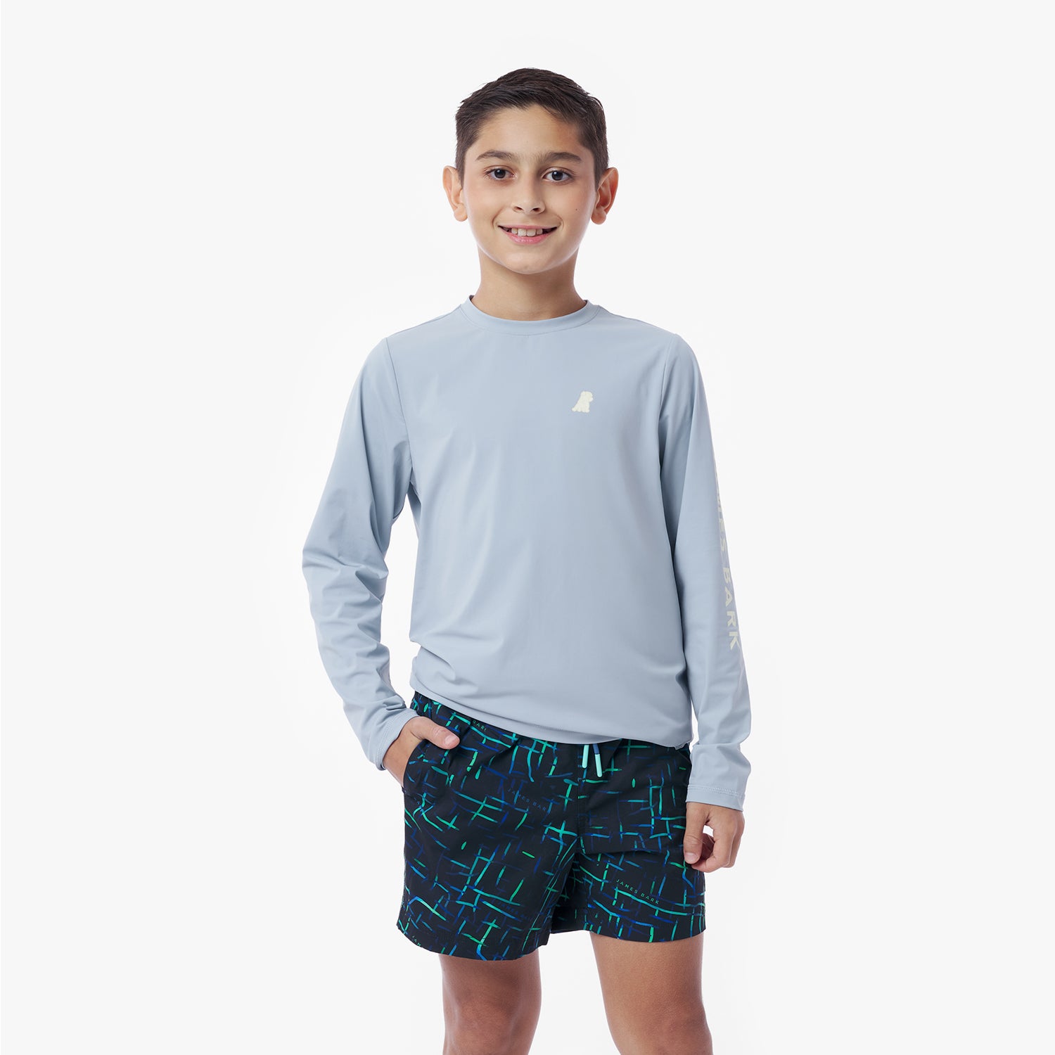 Child wearing a light blue long-sleeve rashguard and dark blue shorts with a pattern on a white background