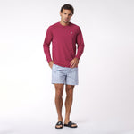 Man wearing a red long-sleeve rashguard and light blue striped shorts on a white background