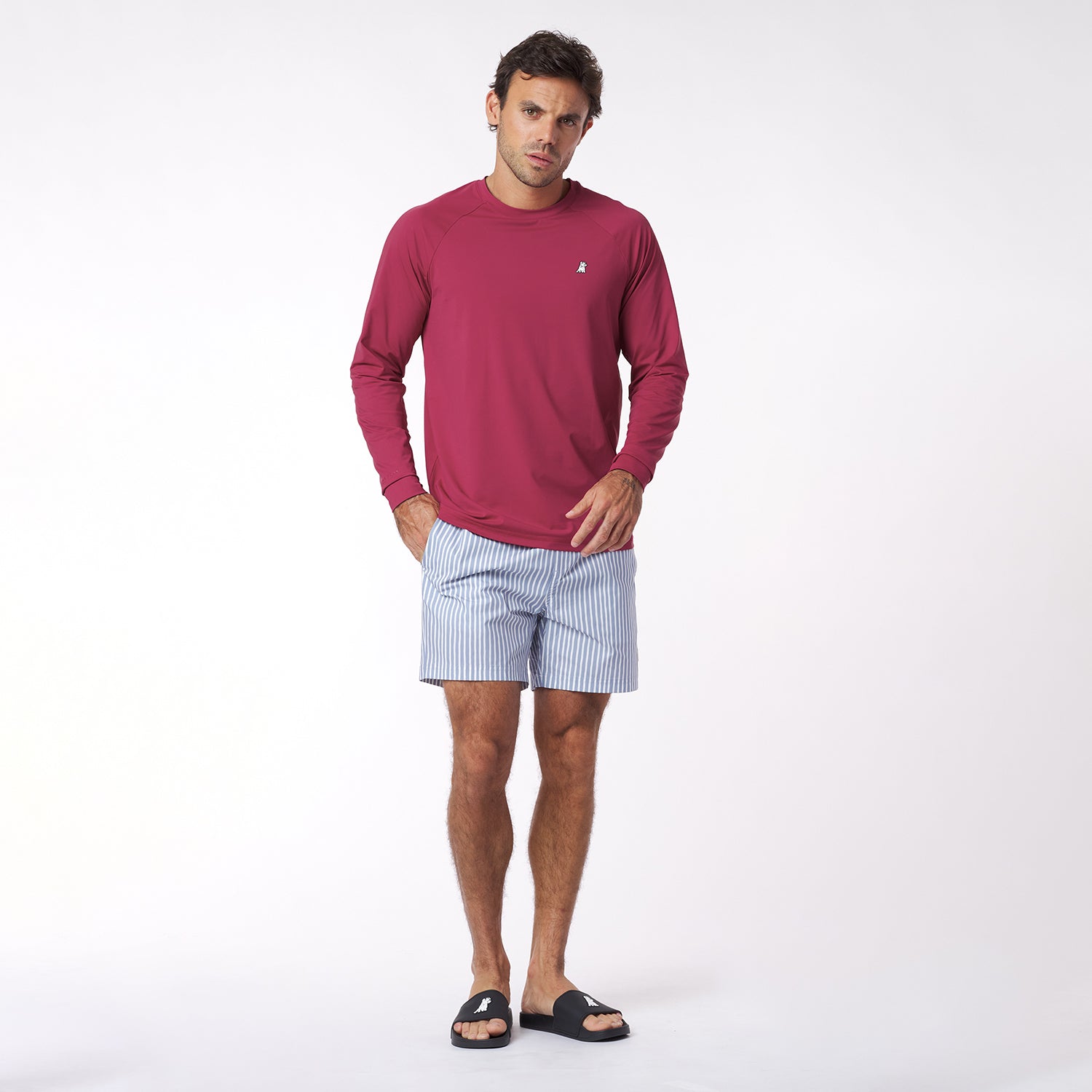 Man wearing a red long-sleeve rashguard and light blue striped shorts on a white background