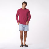 Man wearing a red long-sleeve rashguard and light blue striped shorts on a white background