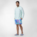 Man wearing a light blue long-sleeve shirt and colorful shorts on a white background