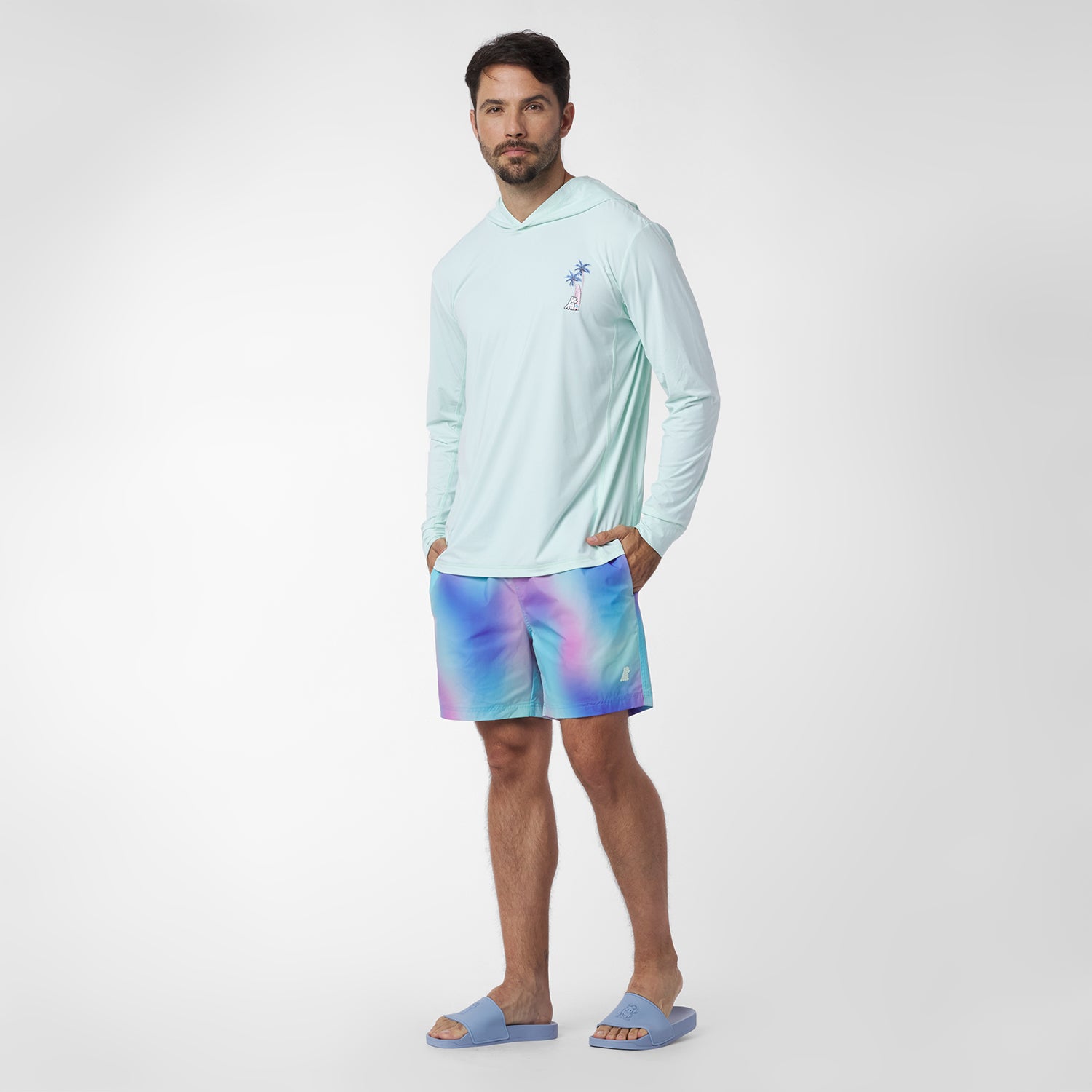 Man wearing a light blue long-sleeve shirt and colorful shorts on a white background