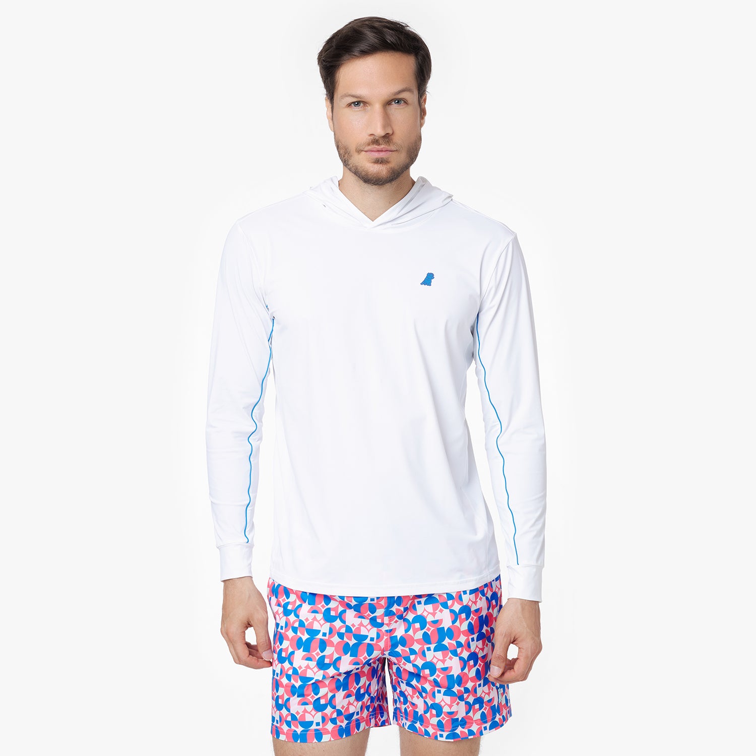 Front view of a man wearing a white long-sleeve hooded shirt with a small blue chest logo, paired with patterned swim trunks