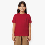 Front view of a young girl smiling, wearing a red t-shirt with a small embroidered logo and brown pants, against a white background