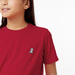 Close-up of a young girl's mouth smiling and the small embroidered logo on her red t-shirt