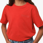 Close-up of the chest area of the red T-shirt, featuring the subtle graphic logo.