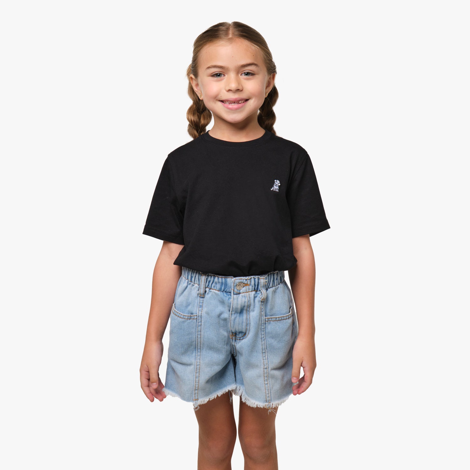 Front view of the girl wearing the black T-shirt with a small embroidered logo on the chest, paired with denim shorts.