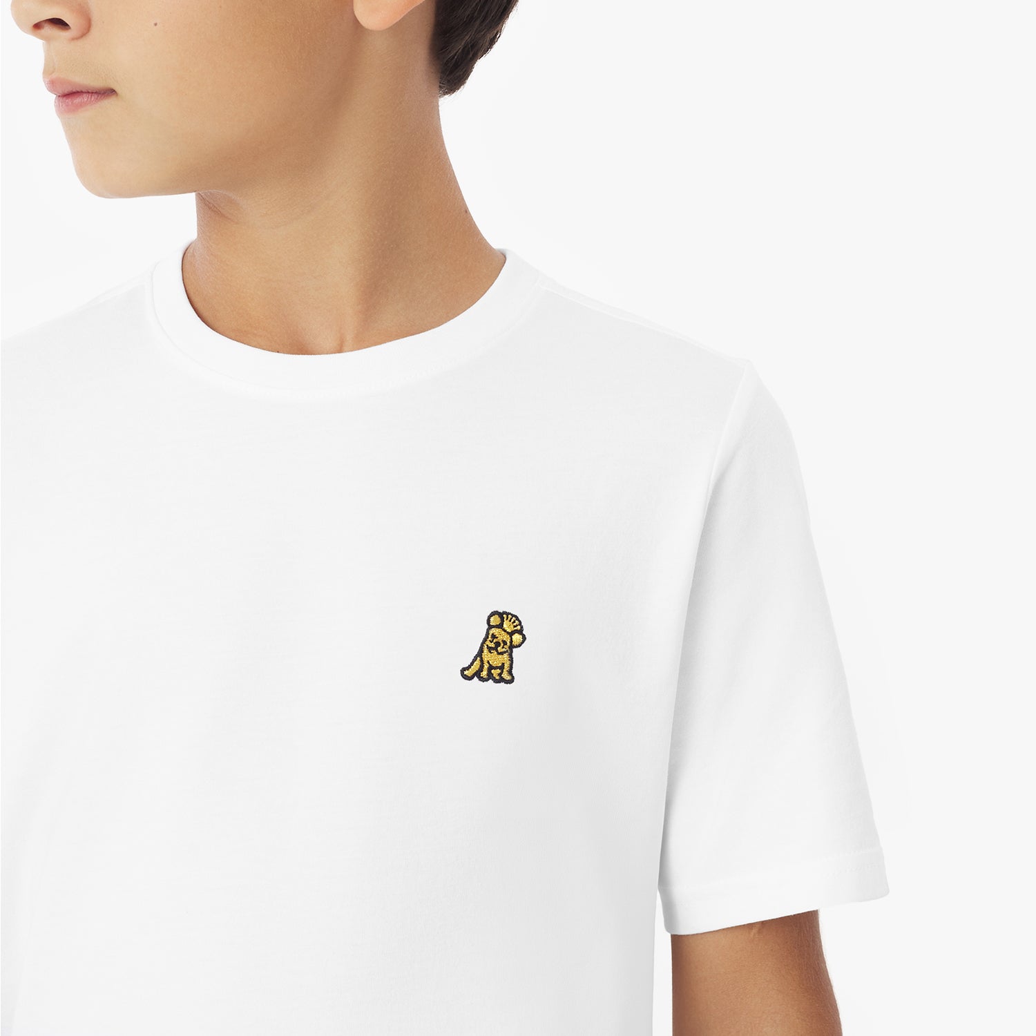 Close-up of a young boy wearing a white t-shirt, showing the small yellow embroidered logo on the chest
