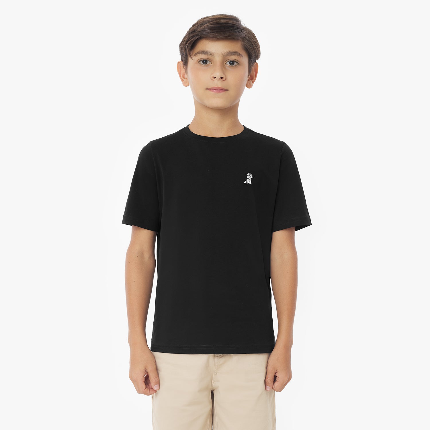 Front view of a young boy wearing a black short-sleeved t-shirt with a white logo and khaki shorts, standing against a white background