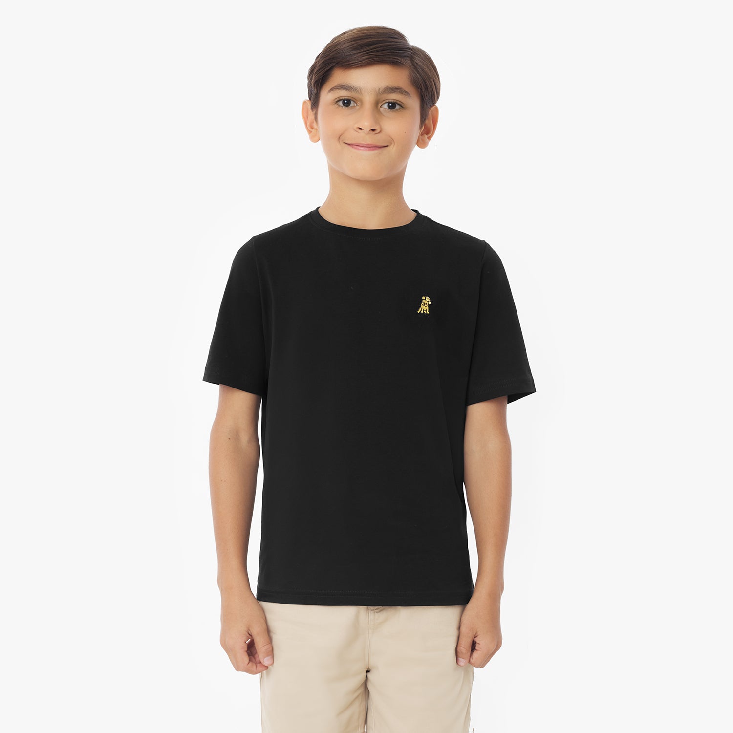 Front view of a young boy wearing a black short-sleeved t-shirt with a yellow logo and khaki shorts, standing against a white background