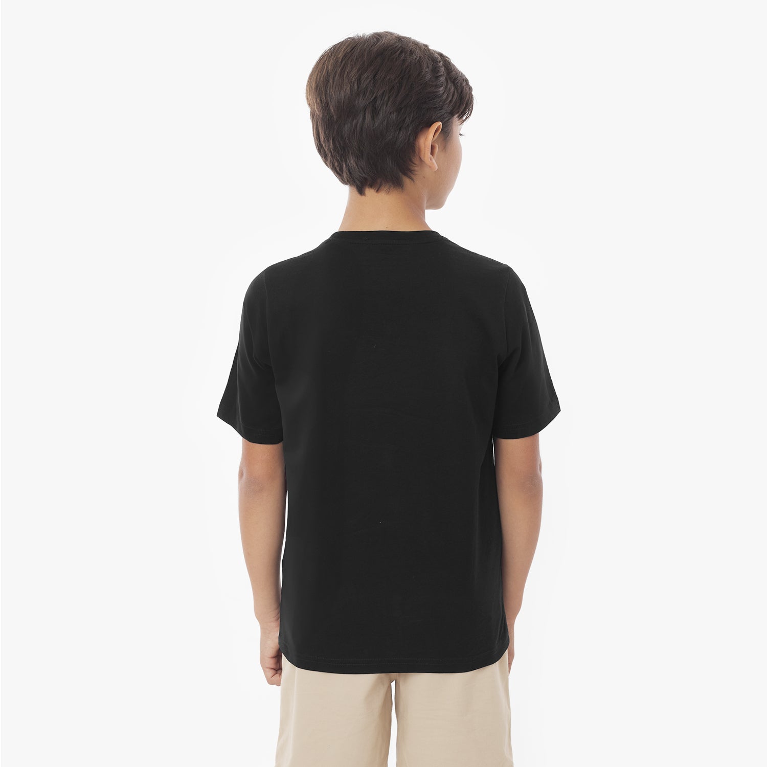 Back view of a young boy wearing a black short-sleeved t-shirt and khaki shorts against a white background