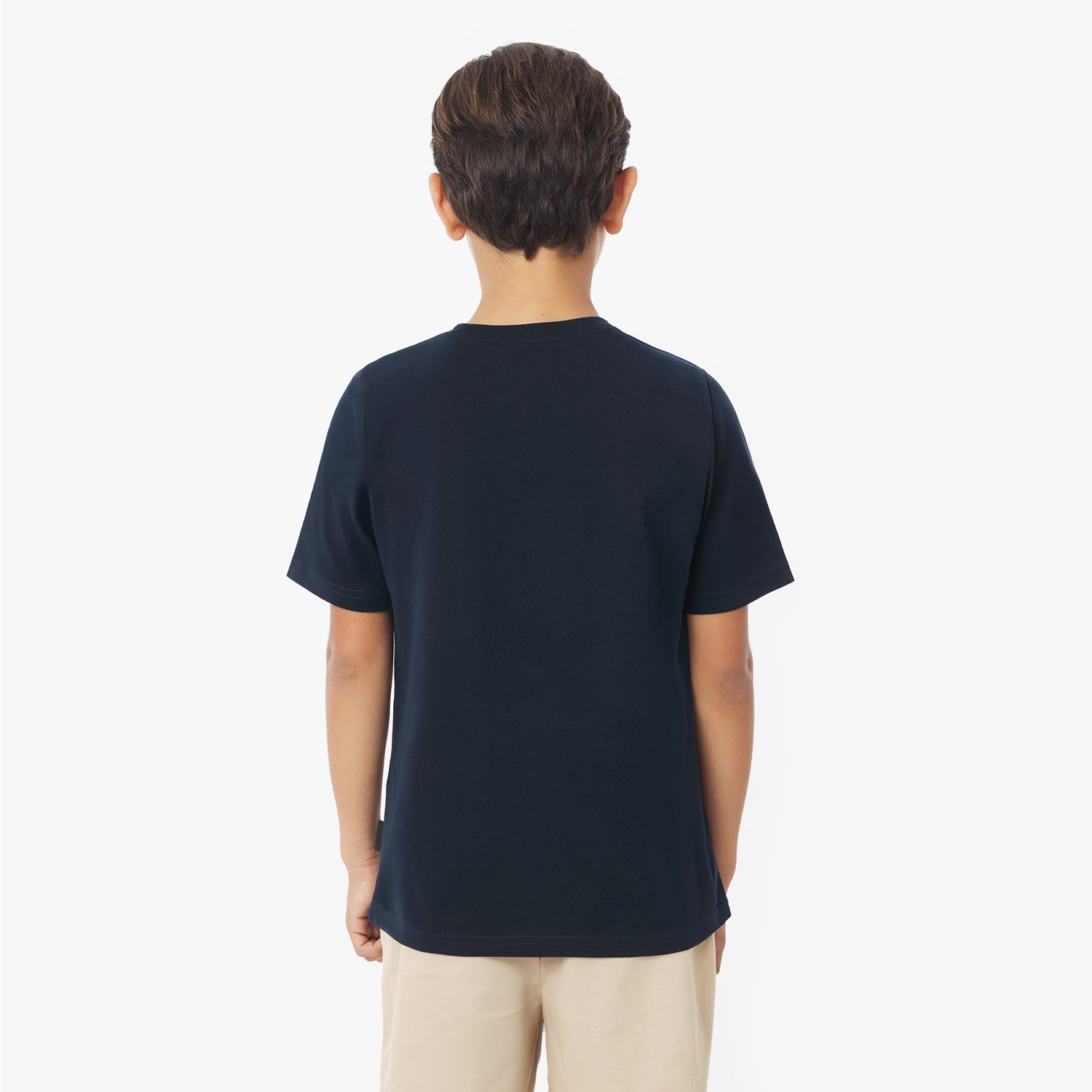 Back view of a young boy wearing a navy blue short-sleeved t-shirt and khaki shorts against a white background