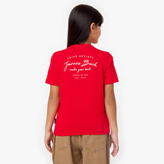 A young girl is seen from the back wearing a red t-shirt featuring white printed text that reads "PRIVÉ SOCIETY, James Bark, make your bark, BASED IN USA, EST. 2015." She pairs the t-shirt with relaxed-fit brown corduroy pants. Her long, straight black hair falls past her shoulders, and she stands in a neutral pose against a plain white background.