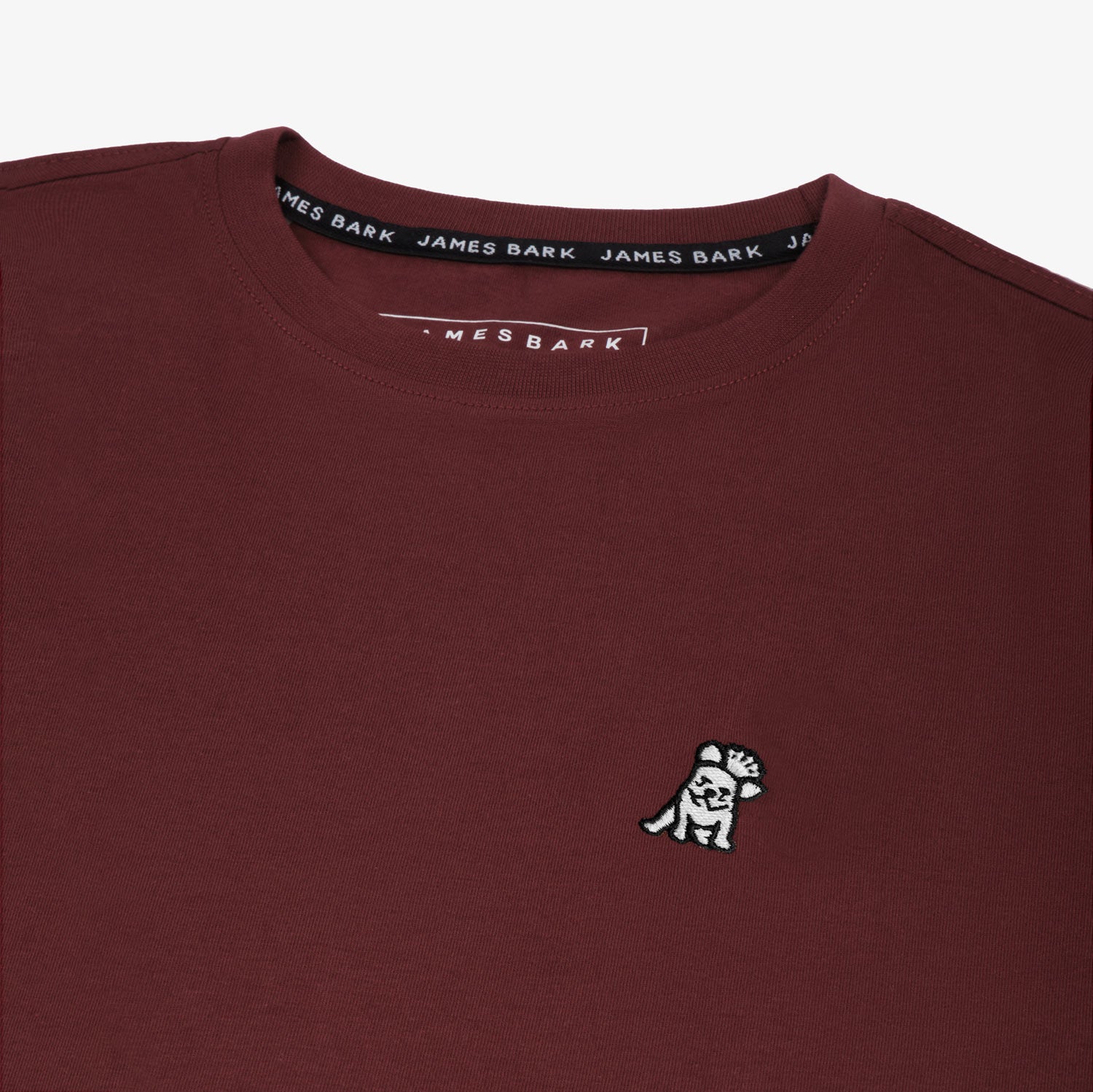 Close-up of the small white embroidered logo on the front of the maroon t-shirt.