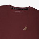 Close-up of the small yellow embroidered logo on the front of the maroon t-shirt.