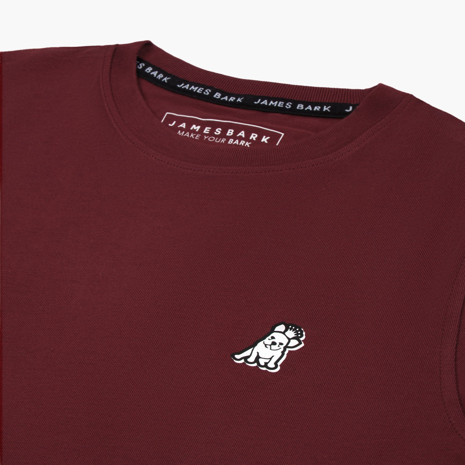 Close-up of the small embroidered logo on the front of the maroon t-shirt.