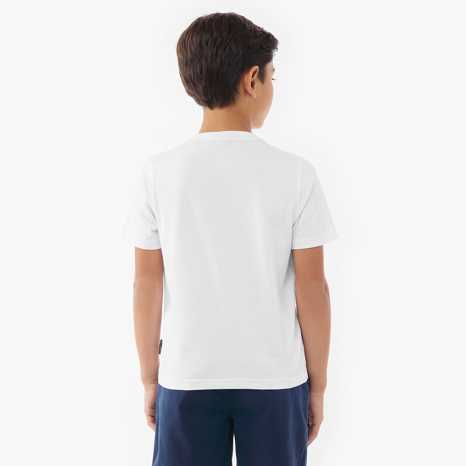 Back view of a young boy wearing a plain white t-shirt and navy blue shorts against a white background