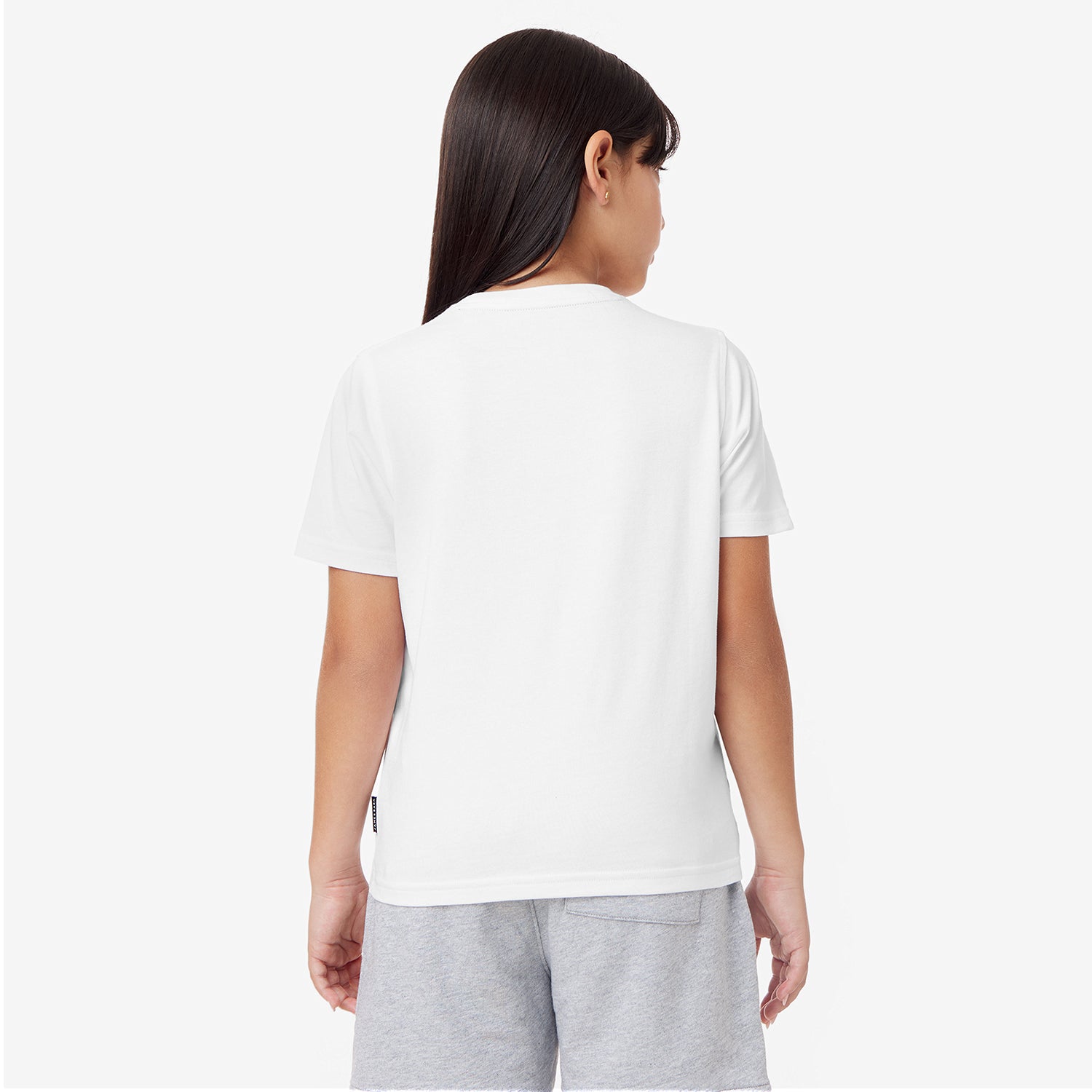 A young girl with long dark hair is seen from the back wearing a plain white t-shirt and light gray shorts. The t-shirt has a relaxed fit with short sleeves, and