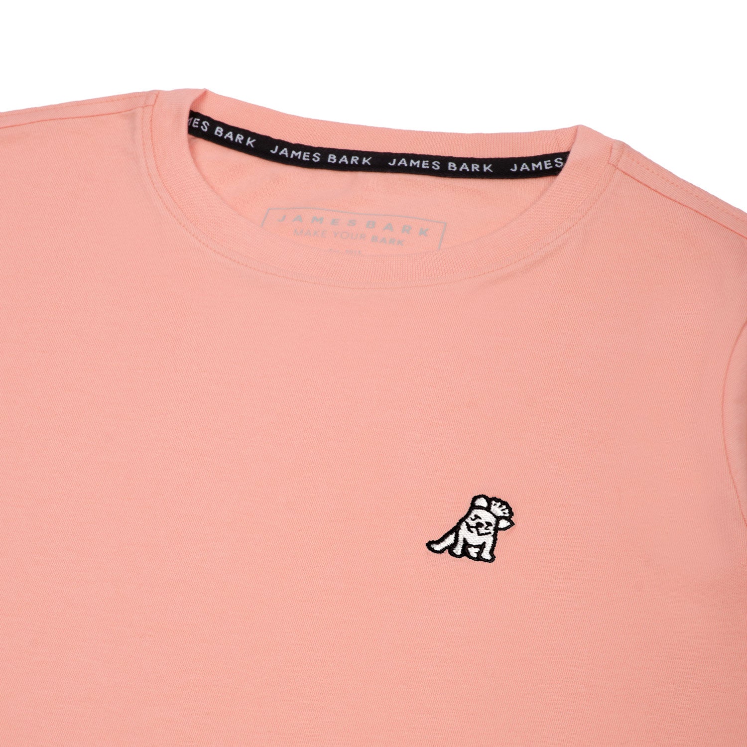 Close-up of the small white embroidered logo on the front of the light pink t-shirt.