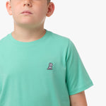 Close-up front view of a boy wearing the mint green t-shirt with a small white embroidered logo on the chest.