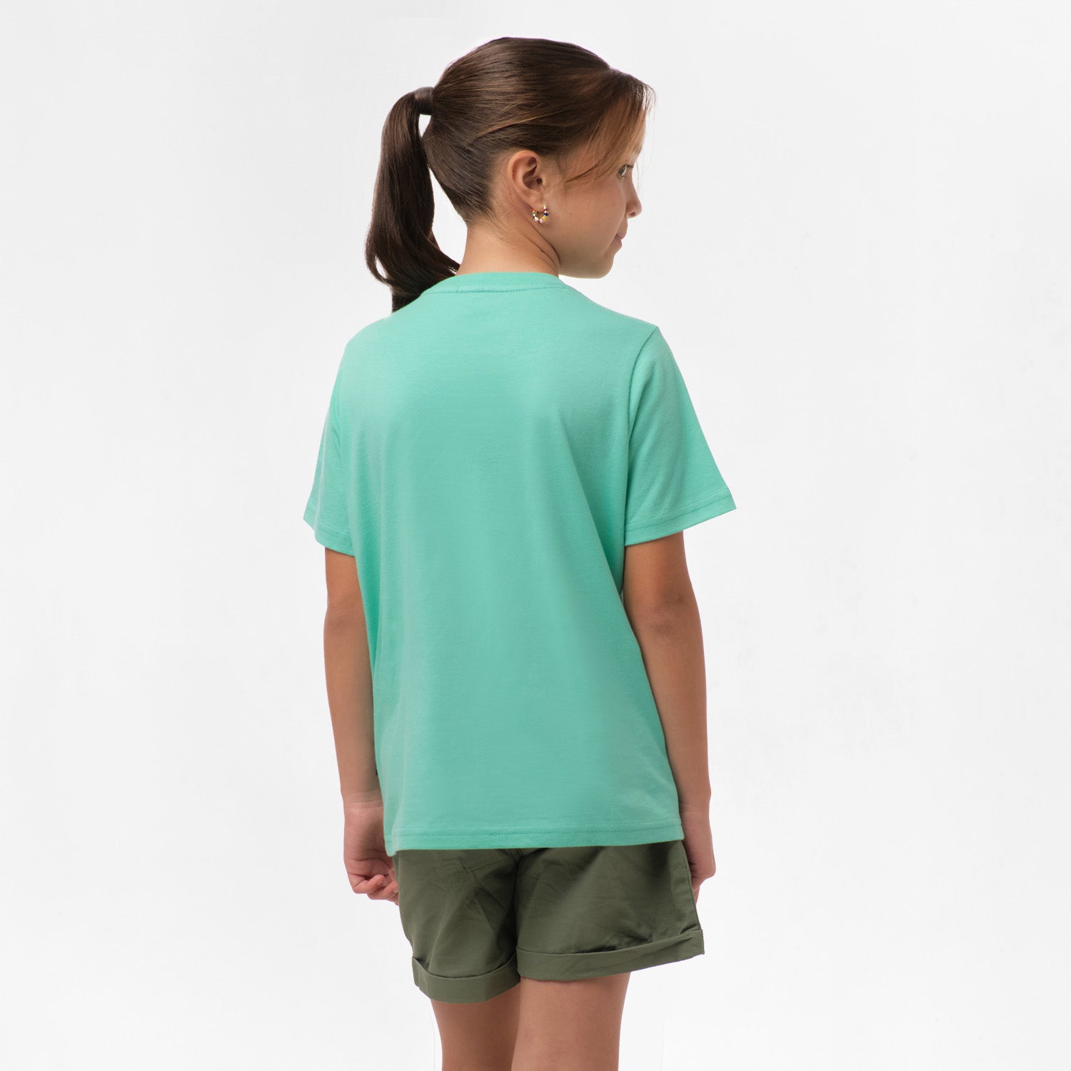 Rear view of a girl wearing the mint green t-shirt, standing with her hands behind her back.