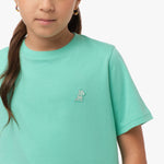 Close-up front view of a girl wearing the mint green t-shirt with a small white embroidered logo on the chest.