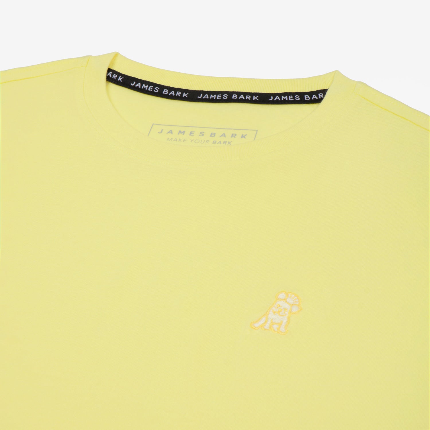 Close-up of the small embroidered logo on the front of the light yellow t-shirt.