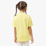 Back view of a young girl wearing the yellow T-shirt with white pants.