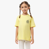 Front view of a young girl wearing a yellow T-shirt with text graphic on the chest, paired with white pants.