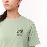 Close-up side view of a woman wearing the light green T-shirt, highlighting the text graphic on the chest.