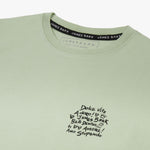 Close-up of the neckline and text graphic on the chest of the light green T-shirt.