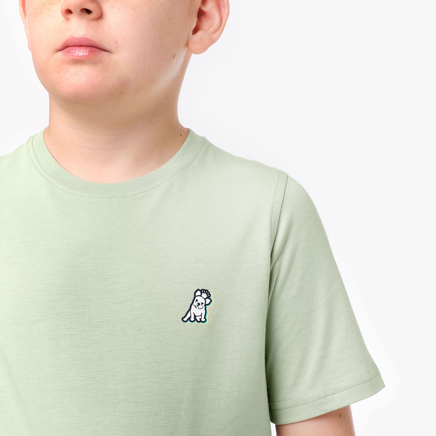 Close-up side view of a boy wearing the light green T-shirt, highlighting the small dog graphic on the chest.