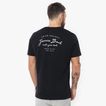 Back view full body shot of a man wearing the black crew neck t-shirt with the large white printed logo, paired with light grey trousers