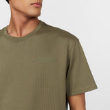 Close-up of a male model wearing an olive green oversized t-shirt. Features an embossed 'JAMES BARK ELEMENTS' logo on the chest, a ribbed crew neckline, and a minimalist design. White background