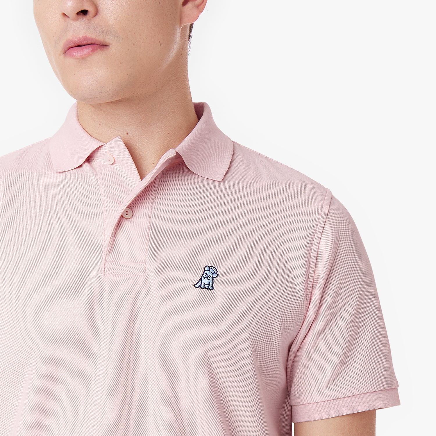 Detailed close-up of the embroidered dog logo on a pink polo shirt