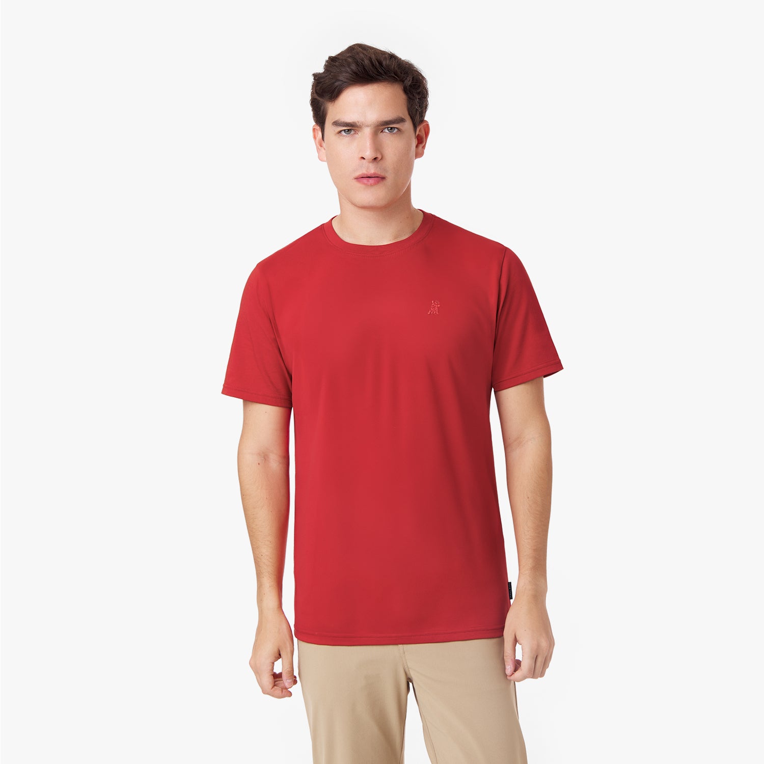 Male model wearing a red short-sleeved t-shirt with a red embroidered dog logo and tan pants, standing front view