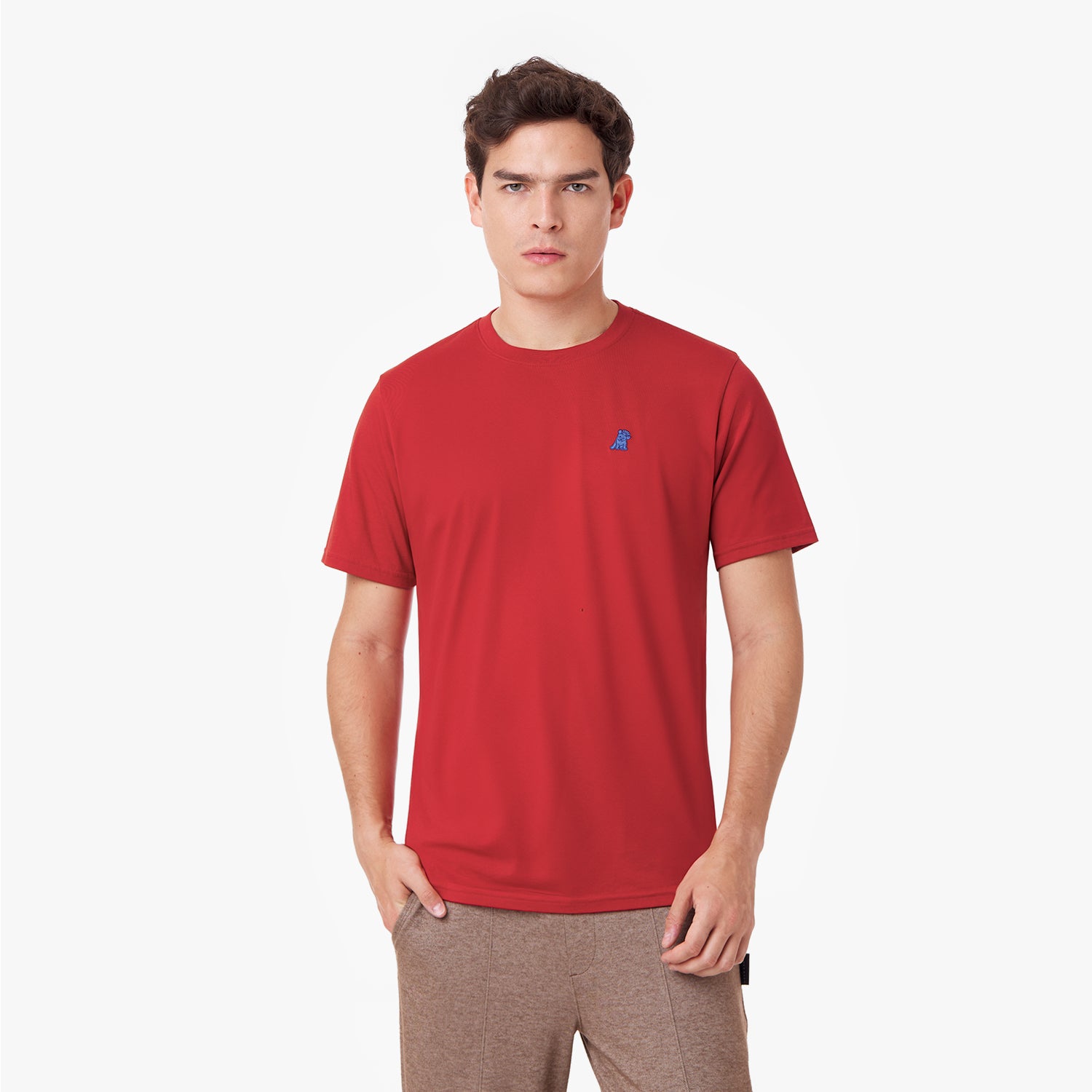 Male model wearing a red short-sleeved t-shirt with a blue embroidered dog logo and brown sweatpants, standing front view with hand in pocket