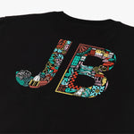 Close-up of the back of a black t-shirt featuring large, colorful 'JB' initials. The letters are filled with intricate illustrations including buildings, waves, gears, and various abstract designs. The vibrant colors and detailed patterns create a bold, eye-catching design.