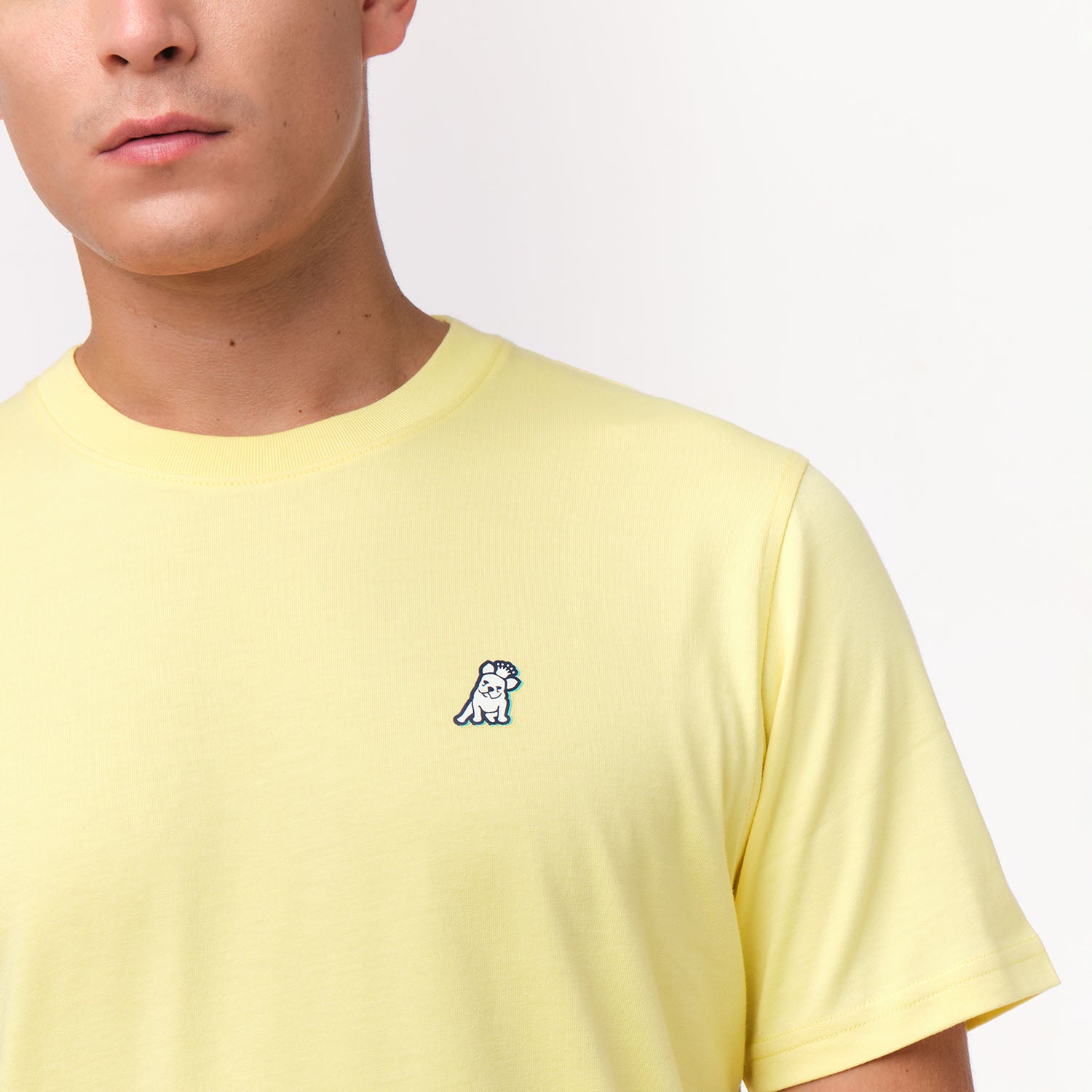 A close-up of the man wearing the yellow T-shirt, focusing on the chest area with the small embroidered dog logo.