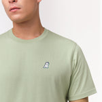 A close-up of the man wearing the light green T-shirt, focusing on the chest area with the small embroidered dog logo.