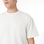 Close-up of a male model wearing an oversized off-white t-shirt. Features an embossed 'JAMES BARK ELEMENTS' logo on the chest, a ribbed crew neckline, and a minimalist design. White background