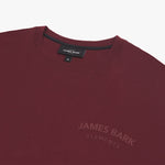 Close-up of a maroon T-shirt featuring a black inner label that reads 'James Bark Elements' and a subtle embossed 'James Bark Elements' logo on the chest. The T-shirt has a ribbed neckline and is displayed against a plain white background." Let me know if you'd like any adjustments